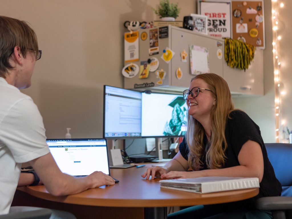 TRiO academic advisor smiling at a student during an in-person meeting at her desk.